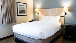 Hotellihuone, jossa on suuri sänky, kaksi yöpöytävalaisinta, yöpöytä ja seinällä oleva kehystetty kuva.