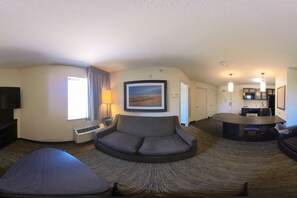 A hotel room with a sofa, a dining table, a TV, and a kitchen area. - Coratel Suites Extended Stay MSP Airport Minneapolis Richfield (Richfield)