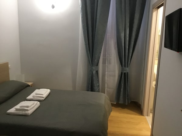 Ein Schlafzimmer mit einem Bett, einem Nachttisch und einem an der Wand befestigten Fernseher.