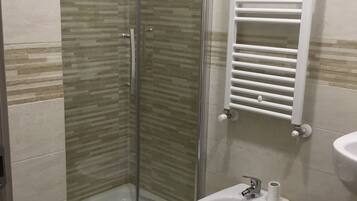 A bathroom with a glass-enclosed shower, a bidet, and a sink with a towel rack above it.