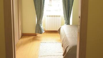 A room with a bed, a window with curtains, a radiator, and a wooden floor.