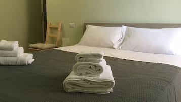 Ein Hotelzimmer mit einem ordentlich bezogenen Bett, einem Holzstuhl und einem Stapel gefalteter Handtücher.