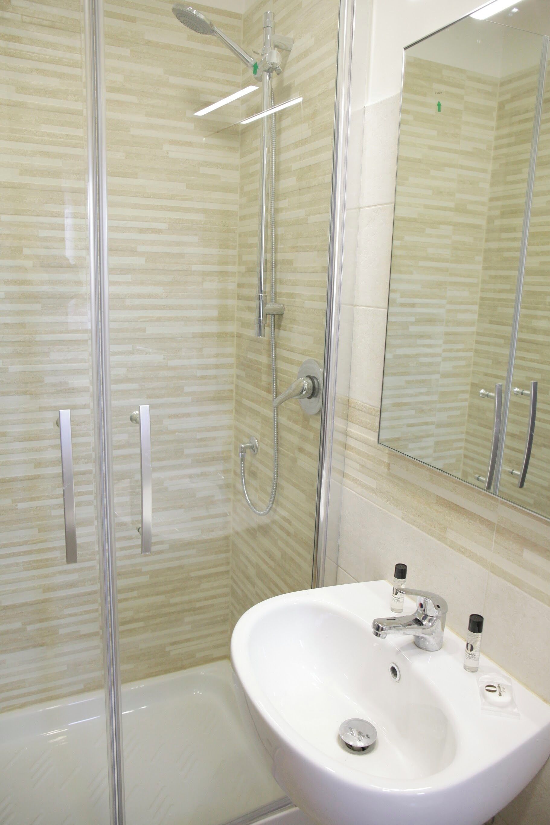 A modern bathroom with a glass-enclosed shower, a white sink with a mirror above it, and a tiled wall.