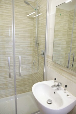 Ein modernes Badezimmer mit einer gläsernen Dusche, einem weißen Waschbecken mit Spiegel darüber und einer gefliesten Wand.