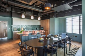 A modern kitchen with a central island, bar seating, and a dining area with a large table and chairs. - One-bedroom | Gym, CoWorking, Library | StayCozy (Croydon)