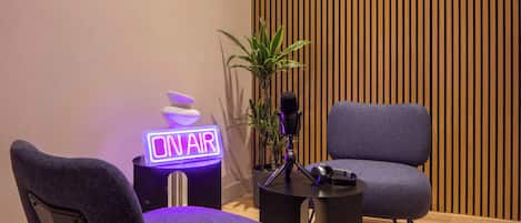 A modern room with a neon sign reading "ON AIR," a microphone on a stand, and two grey chairs.