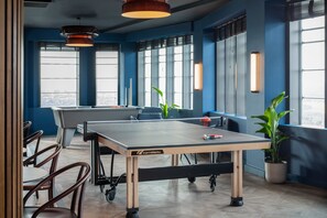A ping pong table in a room with large windows, chairs, and potted plants. - Central Croydon Studio | 40+ Amenities | StayCozy (Croydon)