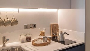 A modern kitchen with a stainless steel sink, a coffee maker, and a book titled "World Atlas of Coffee". - Central Croydon Studio | 40+ Amenities | StayCozy (Croydon)