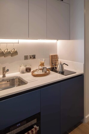 A modern kitchen with a stainless steel sink, a coffee maker, and a book titled "World Atlas of Coffee". - Central Croydon Studio | 40+ Amenities | StayCozy (Croydon)