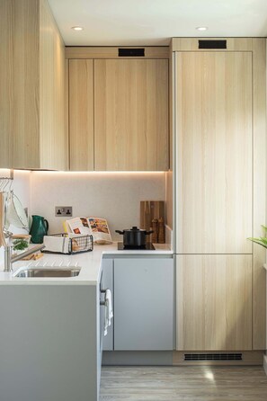A modern kitchen with wooden cabinets, a white countertop, and a built-in oven. - Roomy Studio | Workspace & Laundry Room | StayCozy (Croydon)