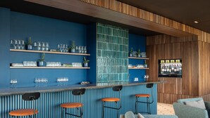 Een bar met blauwe wanden, houten lambrisering en barstoelen. Planken bevatten glazen en potplanten.