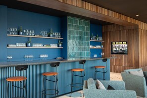 A bar area with blue walls, wooden paneling, and bar stools. Shelves hold glasses and potted plants. - Roomy Studio | Workspace & Laundry Room | StayCozy (Croydon)