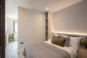 A modern bedroom with a bed, bedside tables, and a built-in shelving unit. - Comfy Digital Nomad Studio | Gym Access | StayCozy (Croydon)