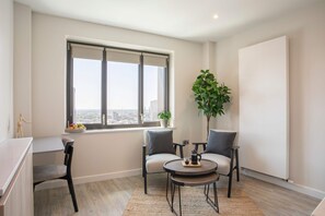 A modern living room with a large window, two chairs, a small table, and a plant. - Comfy Digital Nomad Studio | Gym Access | StayCozy (Croydon)
