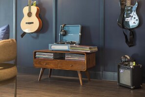 A room with a wooden cabinet, a guitar, a blue case, and a speaker. - Comfy Digital Nomad Studio | Gym Access | StayCozy (Croydon)