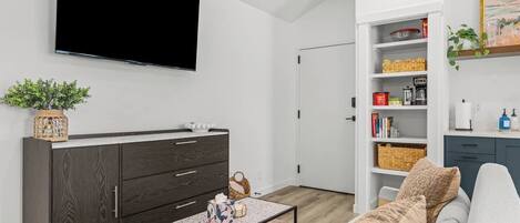 Una sala de estar moderna con un televisor de pantalla plana, un mueble de madera oscura, estantes blancos y un sofá con cojines estampados.
