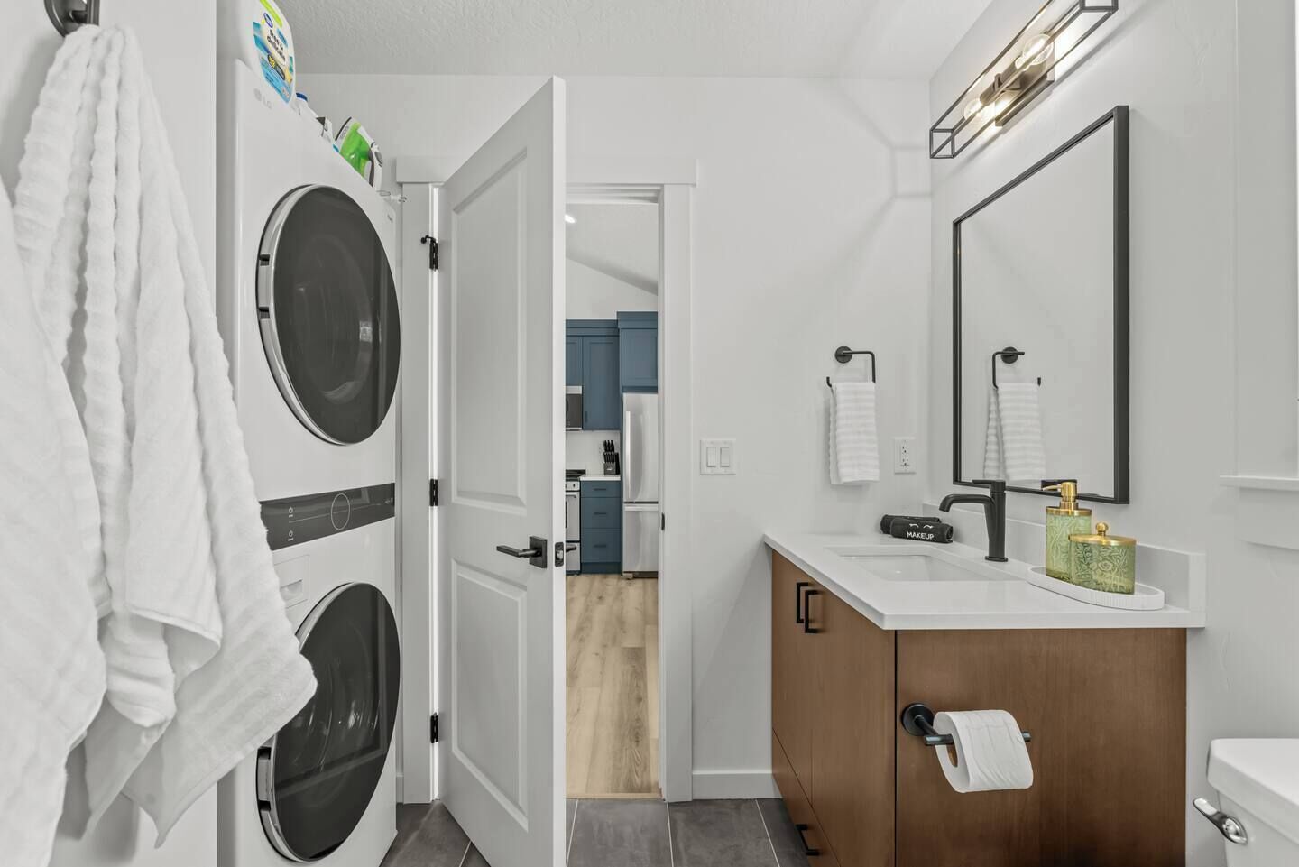 A modern bathroom with a large mirror, a sink, and a toilet. There is a washing machine and dryer in the adjacent laundry room.