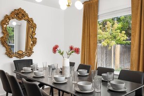 Une salle à manger avec une table dressée pour quatre personnes, un grand miroir décoratif et un vase rempli de fleurs rouges.