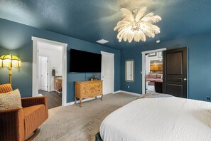 A bedroom with a large bed, a dresser, a TV mounted on the wall, and a ceiling fan. - The High Roller House | Hot Tub & Pool Table (Meridian)