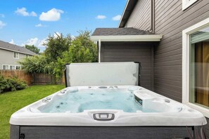 Un jacuzzi dans un jardin, avec une clôture en bois, une maison et un ciel dégagé.