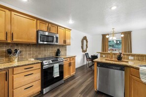 A kitchen with wooden cabinets, a stainless steel microwave, a gas stove, and a dishwasher. - The High Roller House | Hot Tub & Pool Table (Meridian)