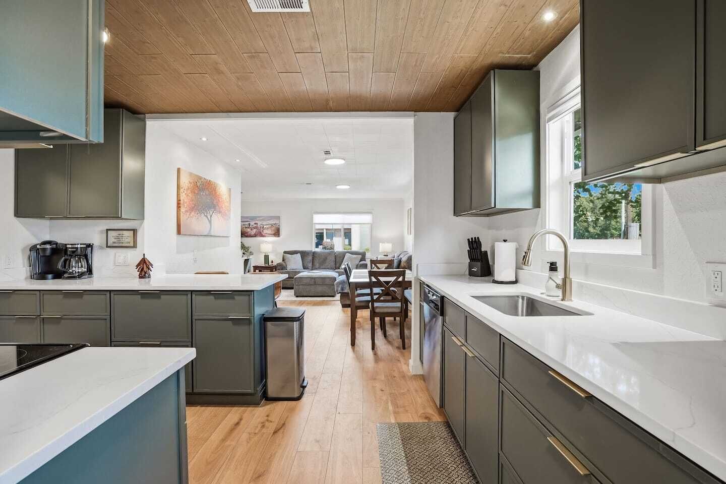 A modern kitchen with a central island, a dining area with a sofa and chairs, and a view through to a living room.