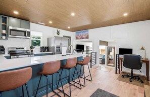A modern kitchen with a large island, bar stools, and a dining area with a TV and seating. - Central Boise Getaway, Walkable, Firepit, Grill, Newly Remodeled (Boise)