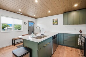 Eine moderne Küche mit einer großen Kochinsel, grünen Schränken und einer Holzbalkendecke.