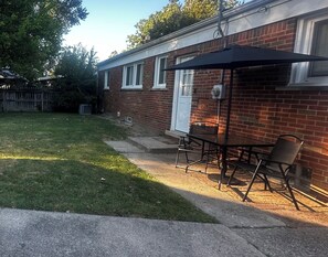 A backyard patio with a table and chairs, a covered area, and a brick house. - Cozy Redford Getaway • Near Detroit & DTW Airport (Redford)