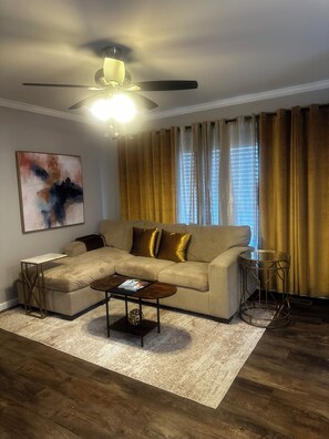 Ein Wohnzimmer mit Ecksofa, Couchtisch, Beistelltisch und Deckenventilator.