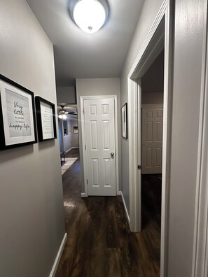 Un couloir avec une porte blanche, des tableaux encadrés accrochés au mur et un luminaire au plafond.