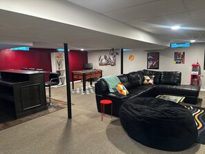 Ein Wohnzimmer mit einem schwarzen Ledersofa, einem schwarzen Sitzsack, einem Kicker und einem roten Sessel.