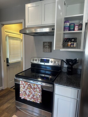 A kitchen with a stainless steel stove, white cabinets, and a variety of spices on the countertop. - Cozy Redford Getaway • Near Detroit & DTW Airport (Redford)
