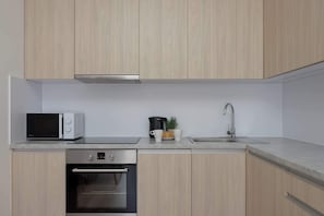 A modern kitchen with light wood cabinets, a built-in microwave, a coffee maker, a sink, and a stainless steel oven. - Stylish Apartment with a Balcony | View of the Skyscrapers (Warszawa)