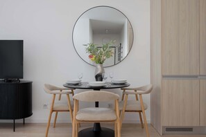 A modern dining area with a round table, two chairs, a vase with flowers, a flat-screen TV, and a cabinet. - Stylish Apartment with a Balcony | View of the Skyscrapers (Warszawa)