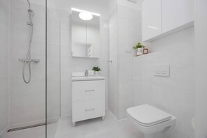 Ein modernes Badezimmer mit einer Duschkabine aus Glas, einem weißen Waschtisch mit Spiegel und einer Toilette.