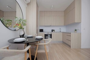 A modern kitchen with light wood cabinets, a black dining table with chairs, and a large mirror on the wall. - Stylish Apartment with a Balcony | View of the Skyscrapers (Warszawa)