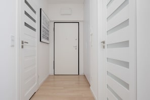 A hallway with a wooden floor, white walls, and doors with frosted glass panels. - Stylish Apartment with a Balcony | View of the Skyscrapers (Warszawa)