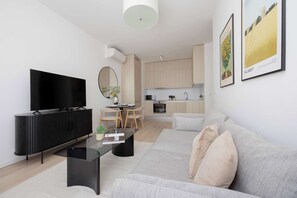 Uma sala de estar moderna com televisão de tela plana, uma mesa de centro preta, um sofá e uma área de jantar com mesa redonda e cadeiras.