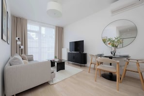 A modern living room with a sofa, a coffee table, a TV, and a dining area with chairs and a table. - Stylish Apartment with a Balcony | View of the Skyscrapers (Warszawa)