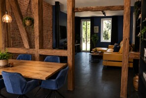 A dining area with a wooden table and blue chairs, a brick wall, and a hanging light fixture.