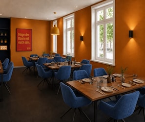 A dining area with tables set for four, blue upholstered chairs, and a red sign on the wall.