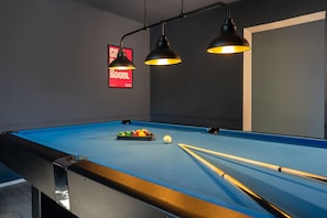 Ein Billardtisch mit Kugeln und Spielstangen, Beleuchtung von oben und ein Schild an der Wand.