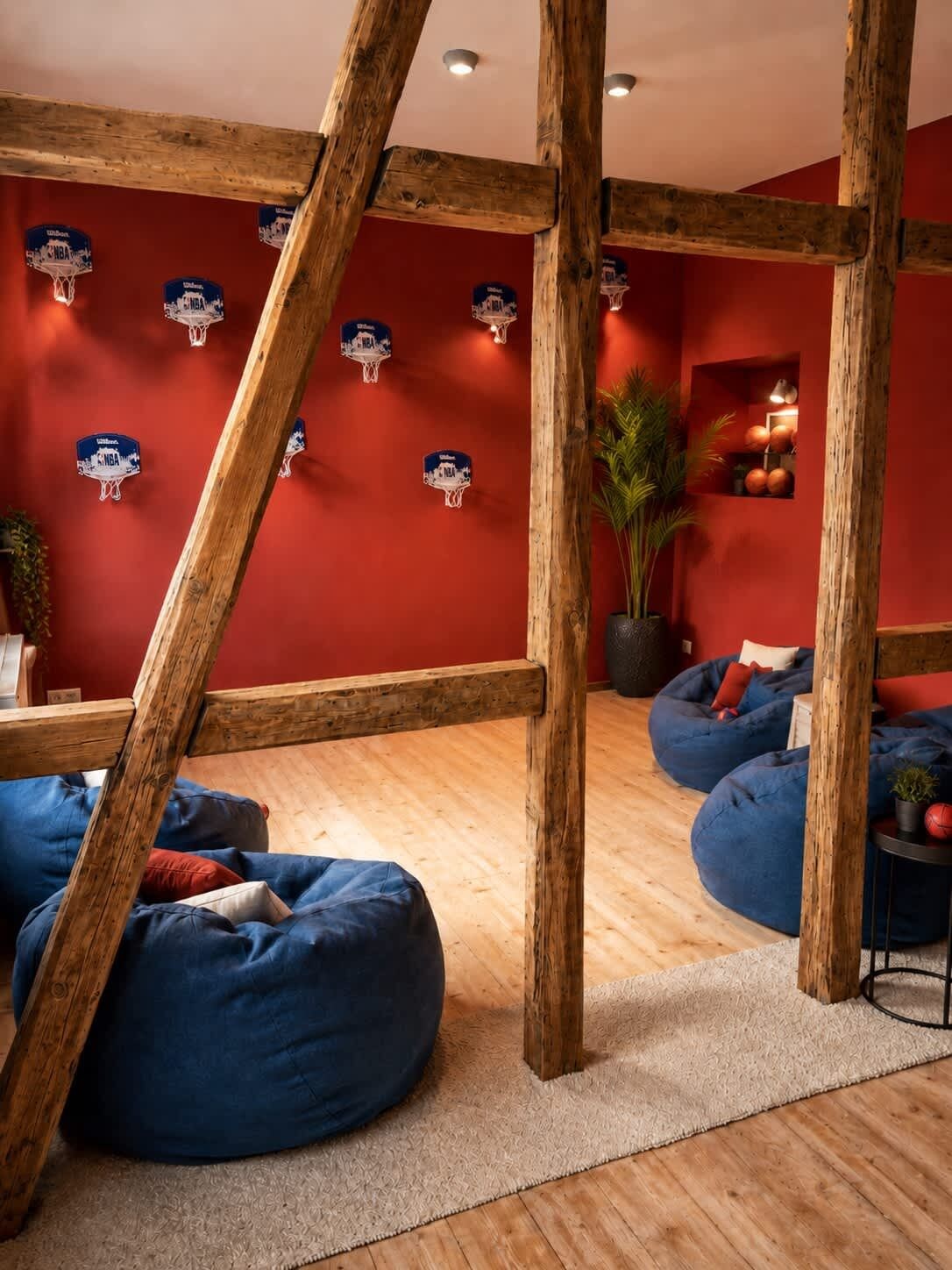 Habitación con vigas de madera, pufs azules, una pared roja decorada con motivos de baloncesto y una planta.