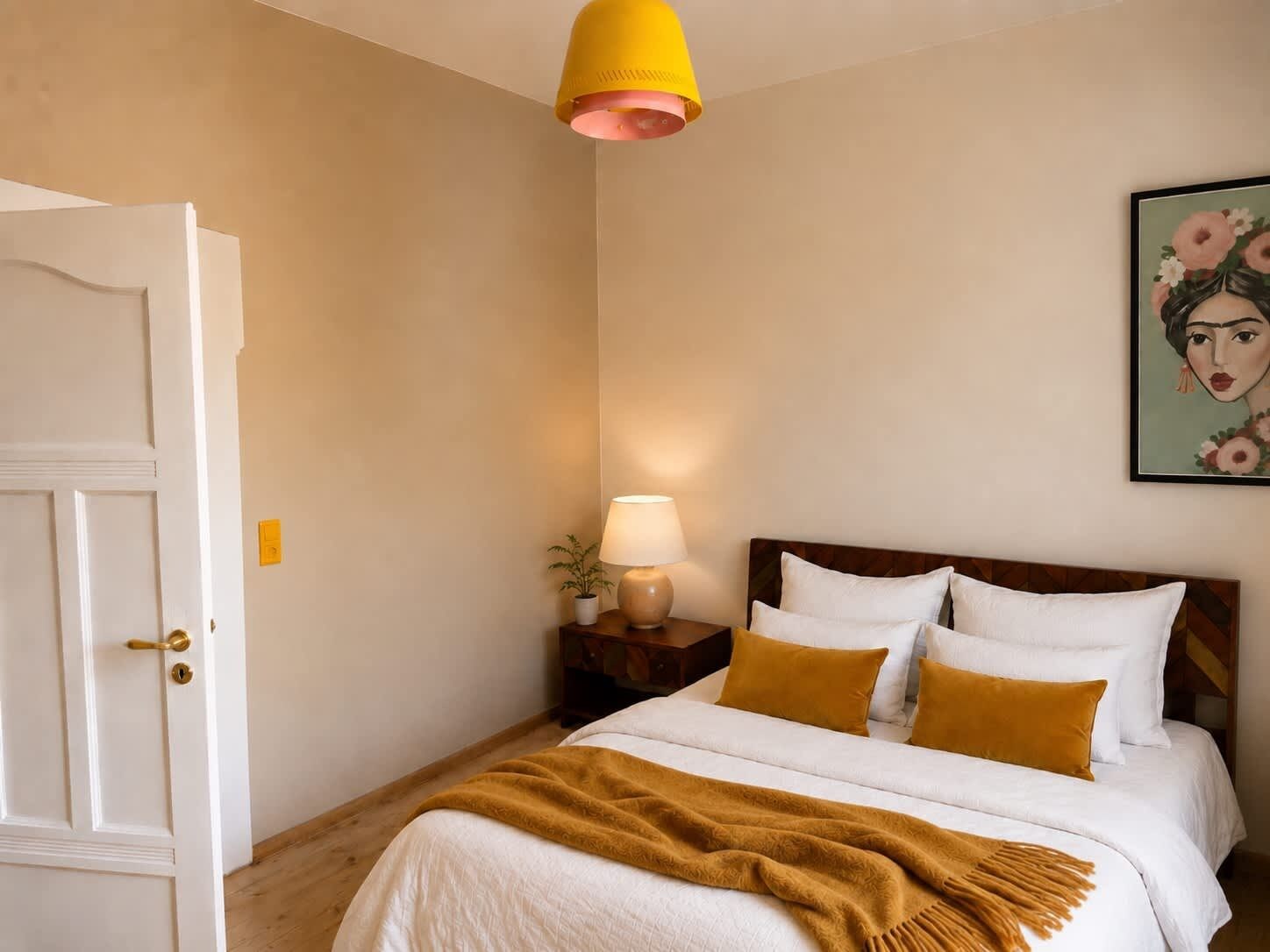 Une chambre à coucher avec un lit, une table de chevet, une lampe, une porte et un tableau au mur.