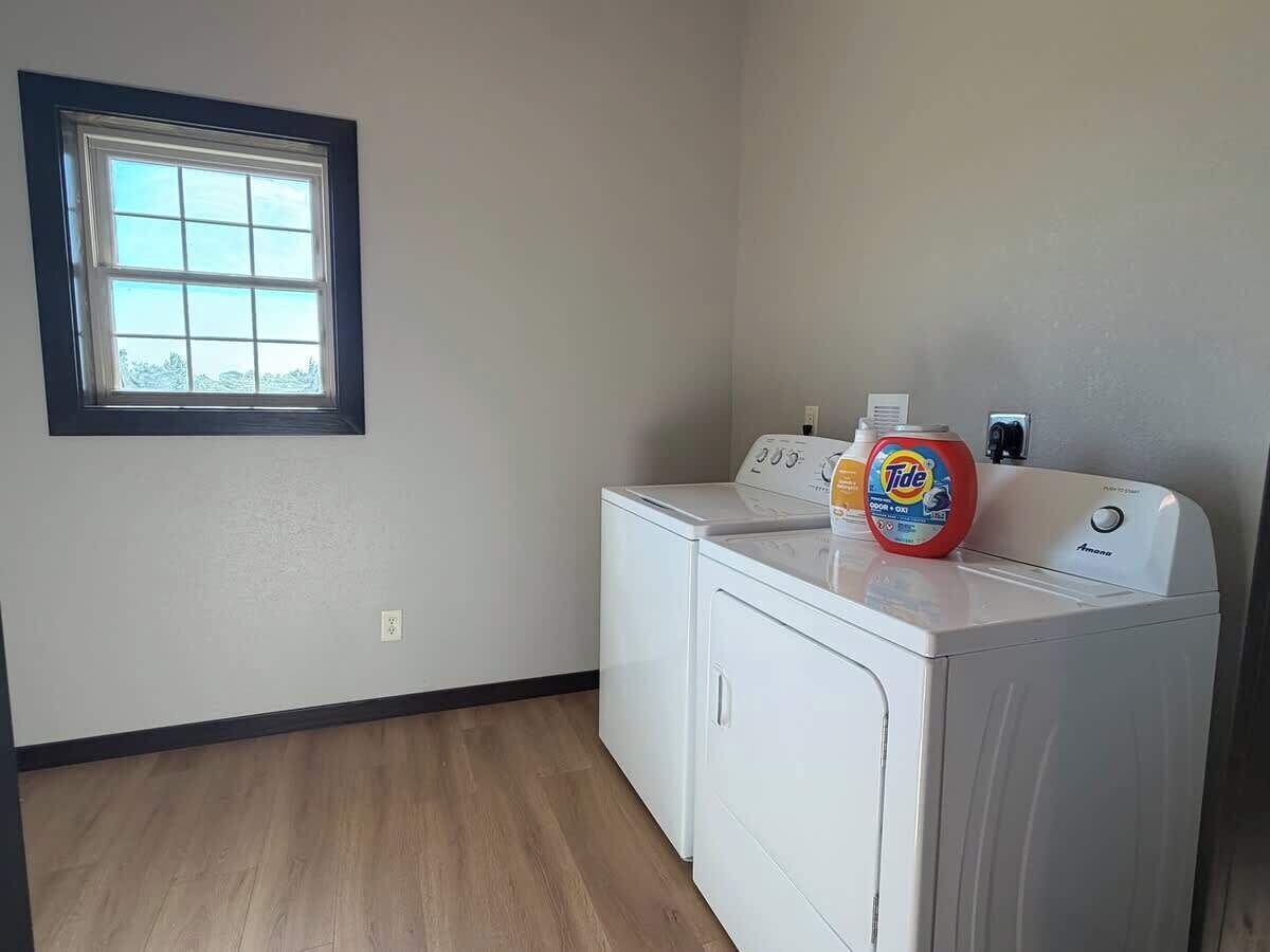 A laundry room with two white washing machines, a Tide detergent bottle, and a window.