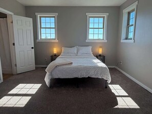 A bedroom with a bed, two bedside lamps, and two windows.
