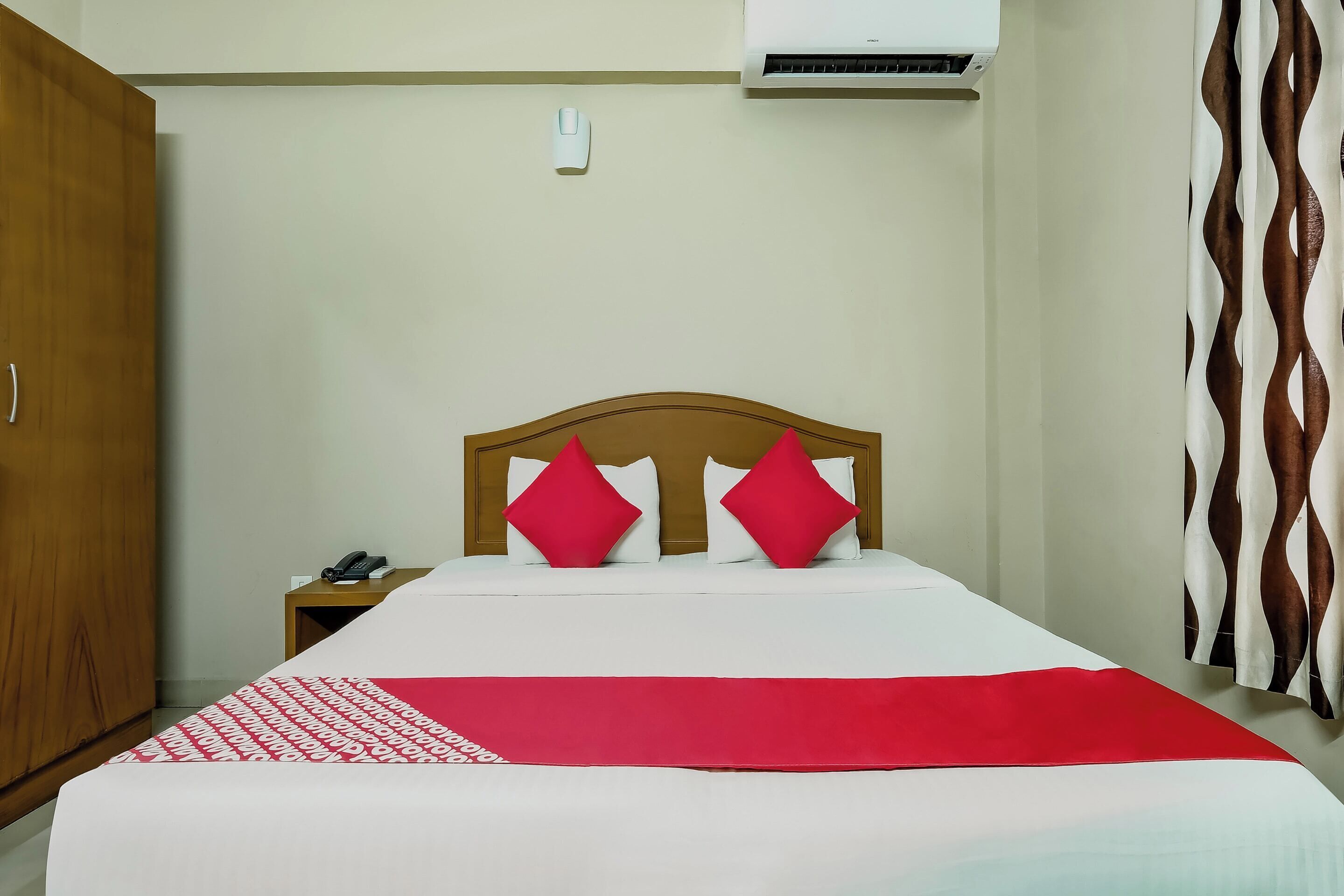 A hotel room with a bed, a nightstand, a telephone, and an air conditioning unit.