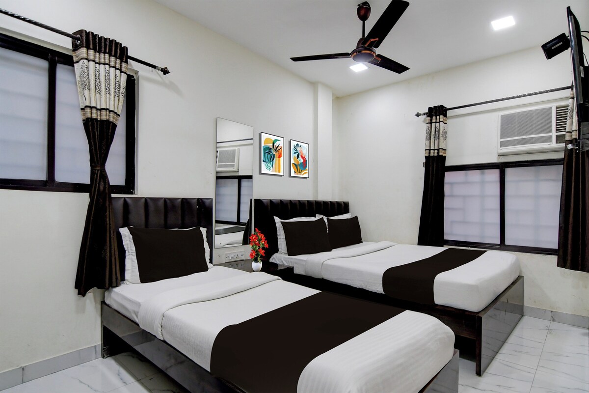A hotel room with two beds, a ceiling fan, a window with curtains, and artwork on the wall.