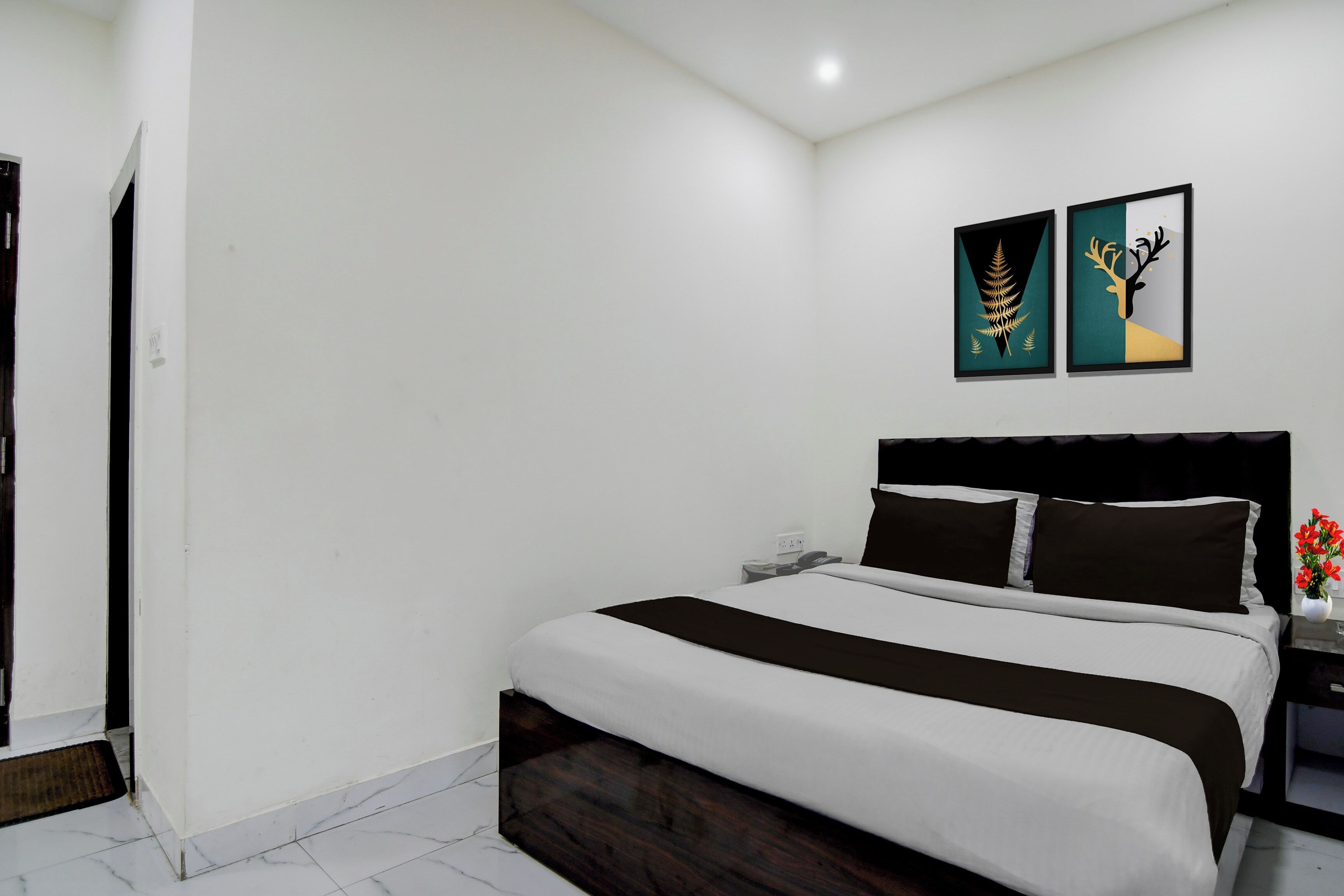Habitación de hotel con cama, mesita de noche, teléfono y dos obras de arte en la pared.